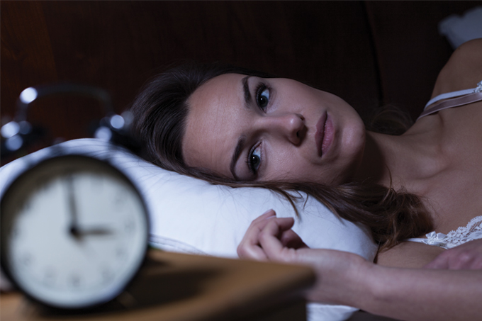 mulher com insônia tentando dormir com relógio à frente