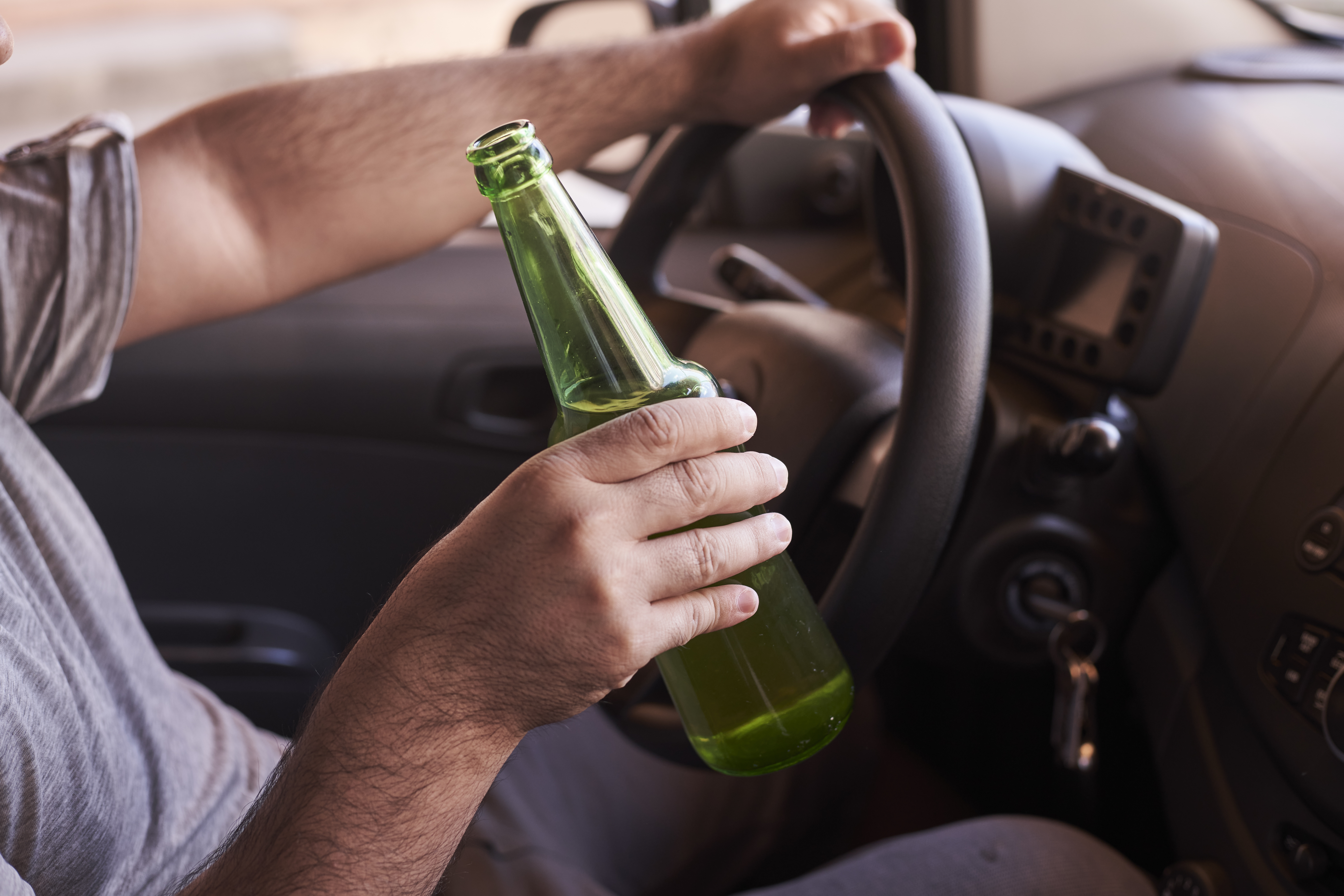 Bottle of beer in a man’s hands driving the car during daytime