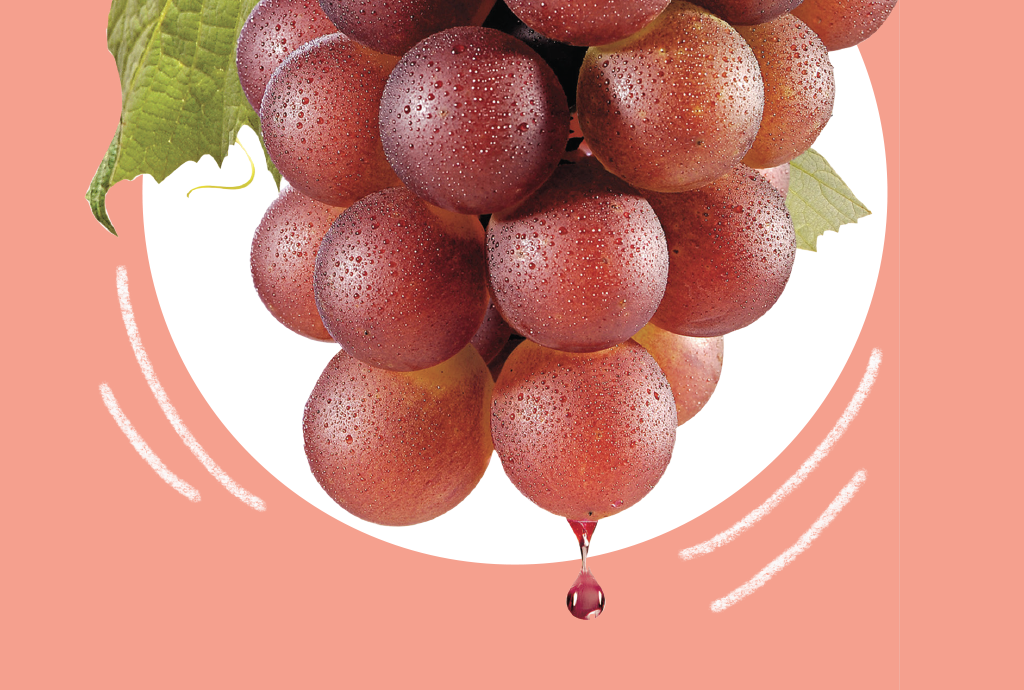 Cacho de uvas vermelhas com gotas de água, uma folha verde e um pingo de suco caindo, sobre fundo rosa e branco
