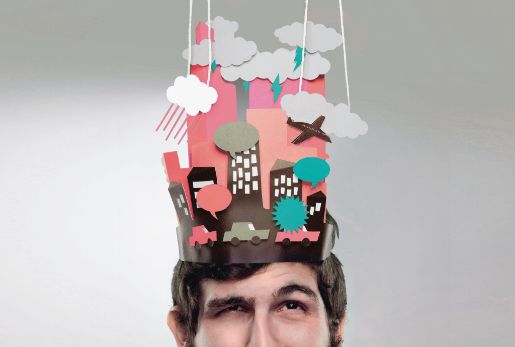 Homem com barba e cabelo escuro, olhando para cima, usando um chapéu de papel que simula uma cidade com prédios, carros, balões de fala, nuvens com chuva e raios, e um avião, sobre fundo cinza